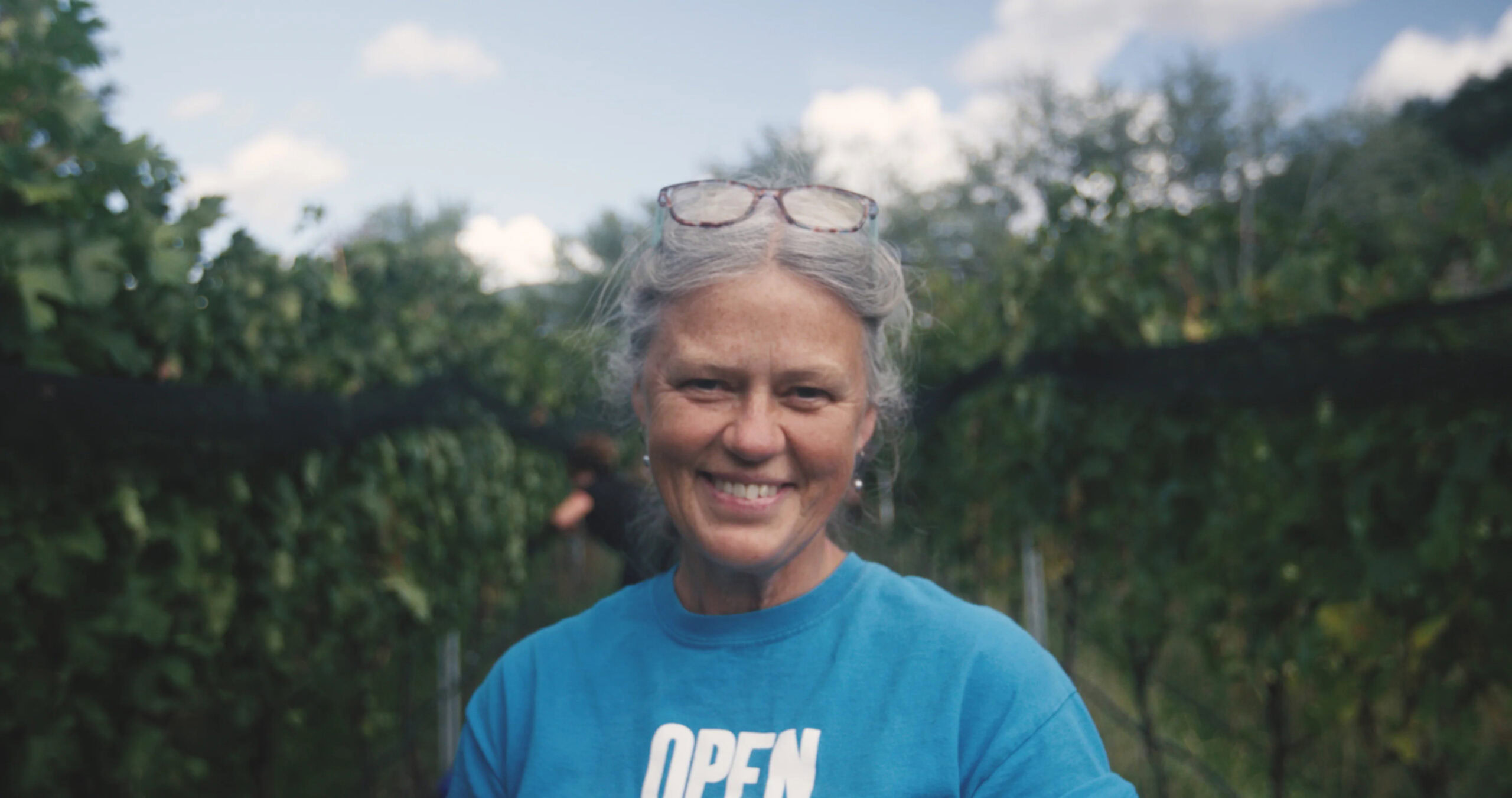 Woman smiling at Echo Bay Vineyard with lush grapevines in the background.